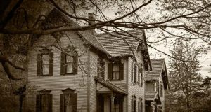 Black and white image of an old house, through tree branches.