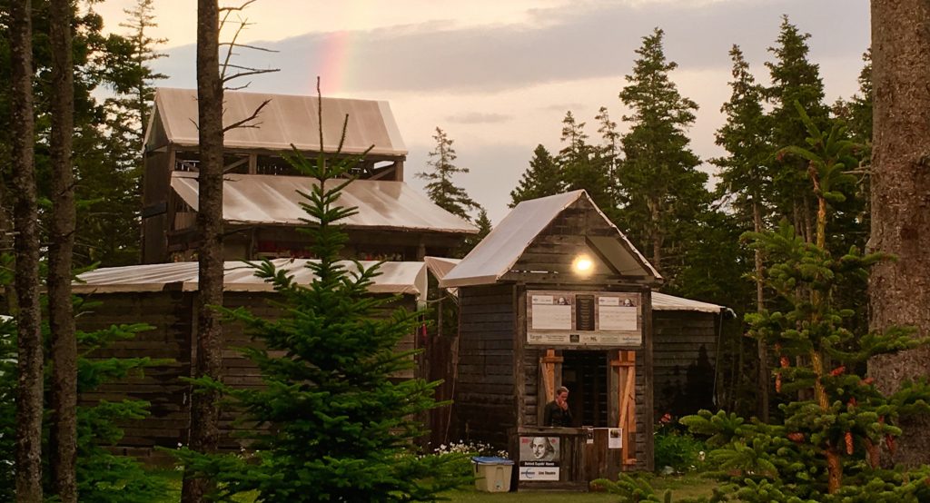 Large wood theatre building in the woods with bright colourful rainbow arching overhead.