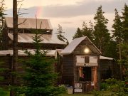 Large wood theatre building in the woods with bright colourful rainbow arching overhead.