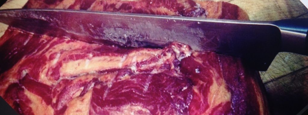 Large butcher knife cutting through bloody steak.