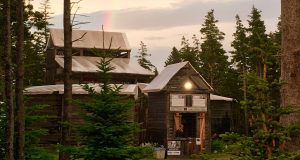 Large wood theatre building in the woods with bright colourful rainbow arching overhead.
