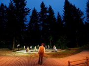 A forest clearing at night. A large cast of actors in tableaux across the clearing, dressed in early 1900s clothing.