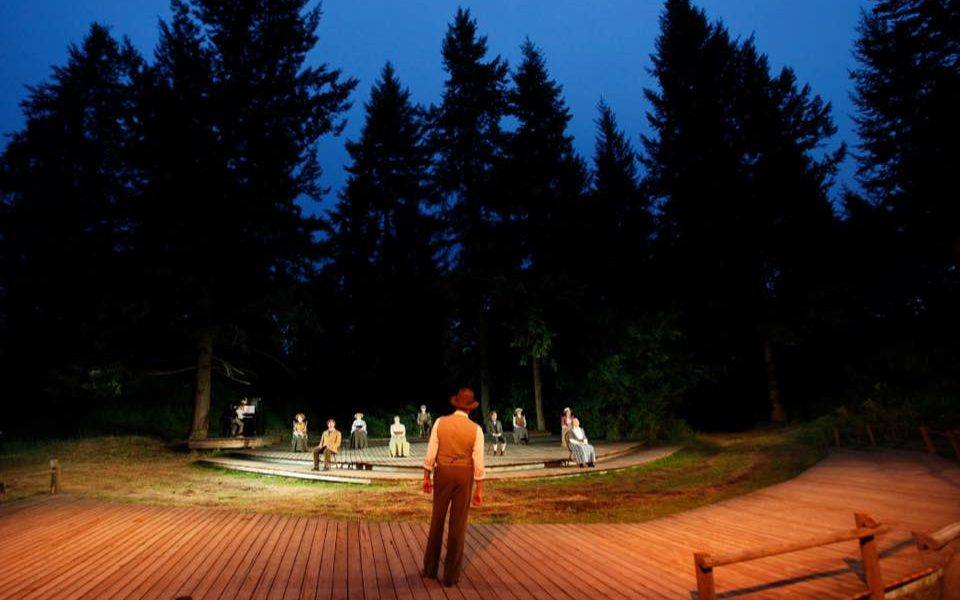 A forest clearing at night. A large cast of actors in tableaux across the clearing, dressed in early 1900s clothing.