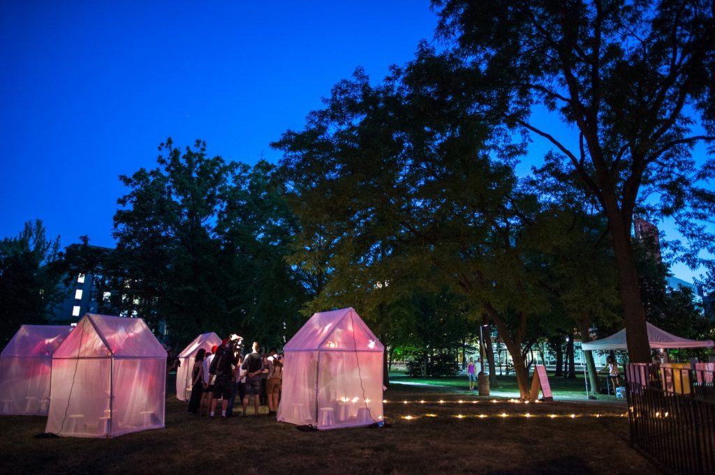 Tents with pink and yellow lights inside. In a grove of trees.