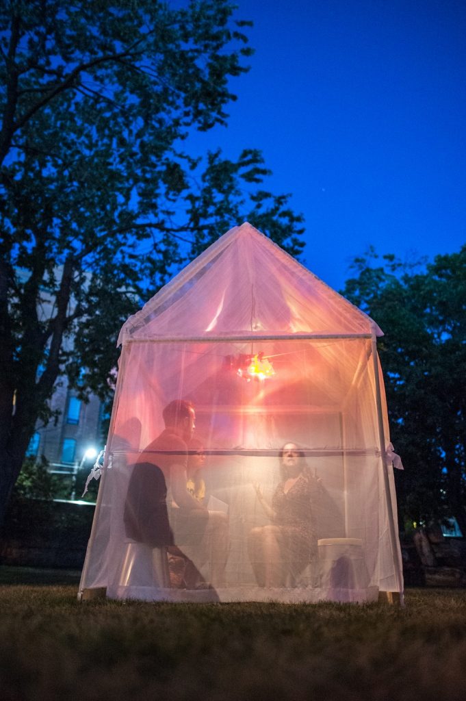 A tent made of clear plastic with pinks and yellow lights inside.
