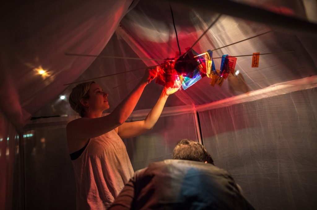 A woman hangs colourful pieces of paper along the inside of a tent.
