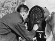 Black and white photo of man tinkering with old time wooden radio.