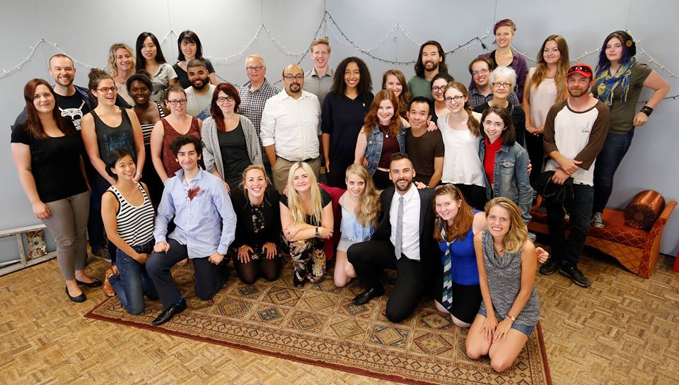 Large team of young artists, standing and kneeling on a big carpet.