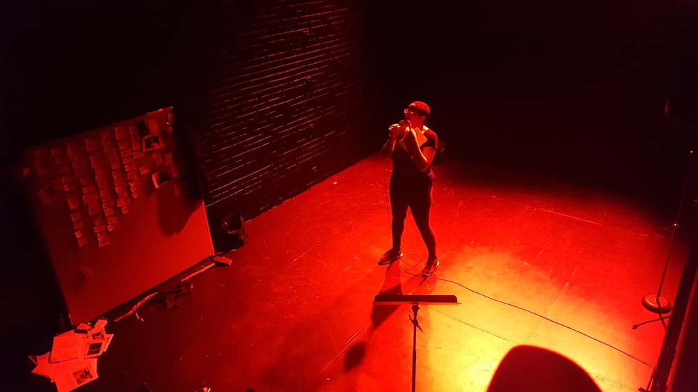 Donna-Michelle performing in the centre of an intimate stage, under red lighting.
