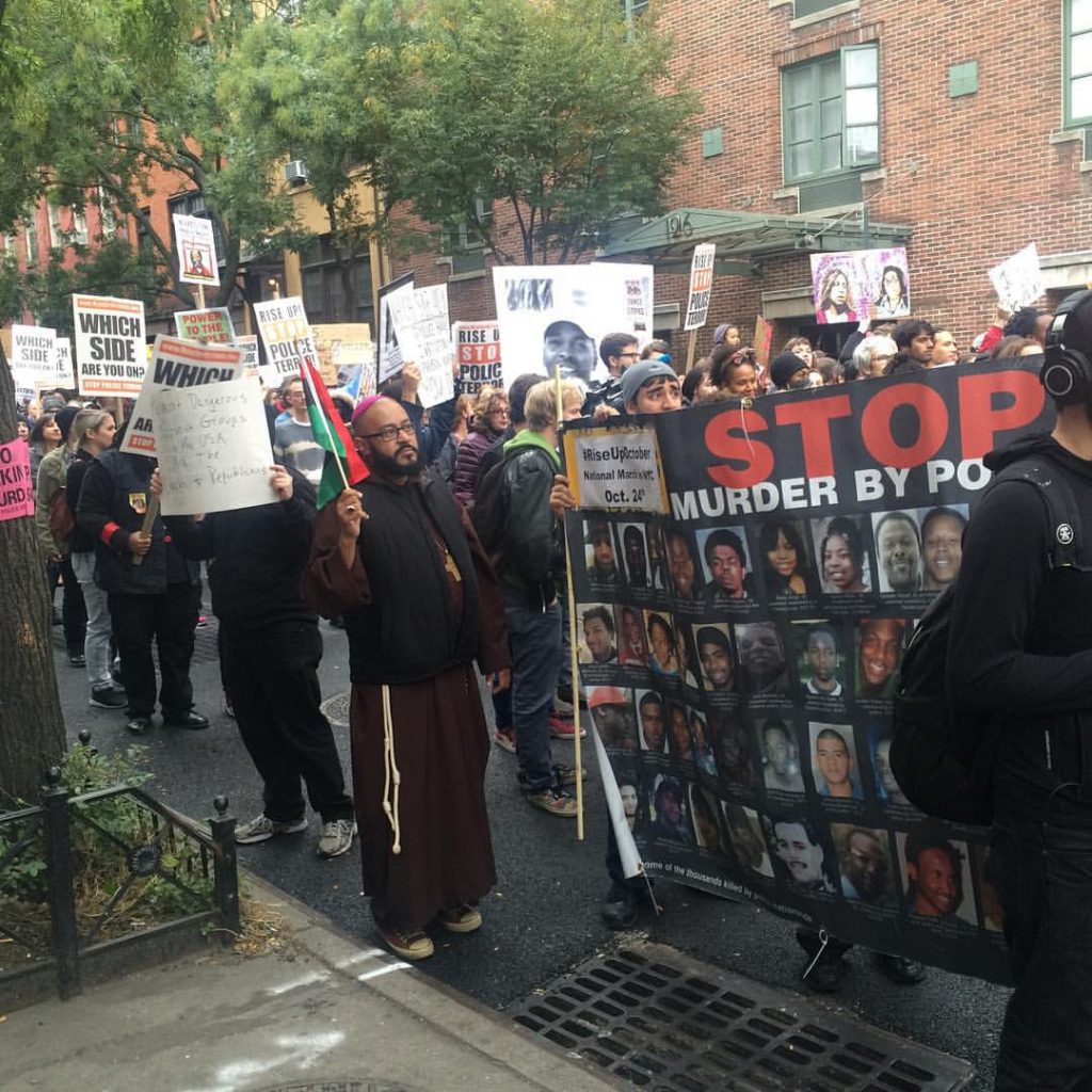 A large group of people walking on a New York street with picket signs and banners reading Stop Murders by Police and Black Lives Matter.
