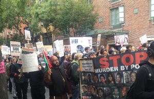 A large group of people walking on a New York street with picket signs and banners reading Stop Murders by Police and Black Lives Matter.