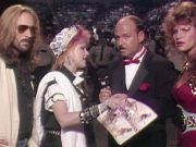 Four figures gathered around a microphone. Cyndi Lauper speaks into the microphone as the other three individuals look at the camera, somewhat surprised.